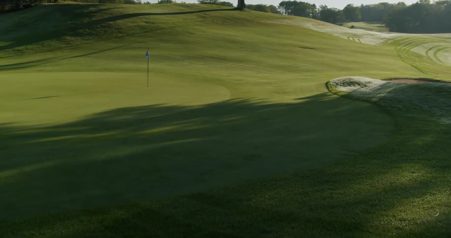 A golf course with tree shadows cast on it and a flag pole on the green