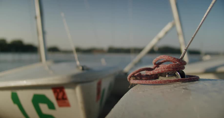 Close up of red rope tied around a cleat on a sailboat at a pier in the morning