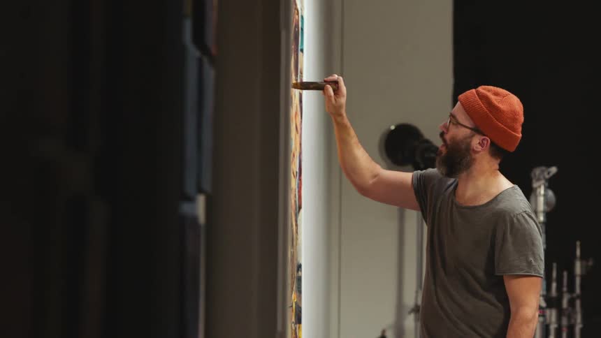 White man wearing beanie in artist studio working on painting