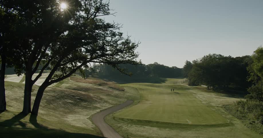 A couple of distant golfers walking on a golf course under a bright sun