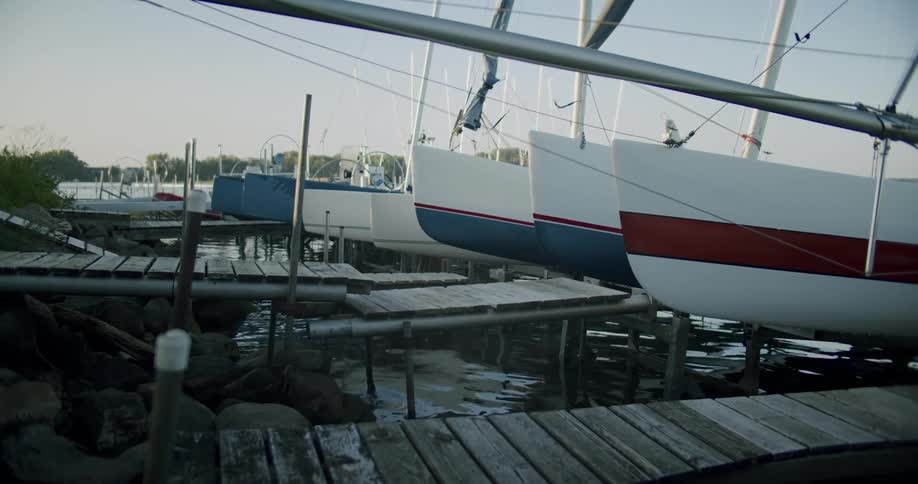 A group of catamarans are docked along short wooden piers on a sunny day