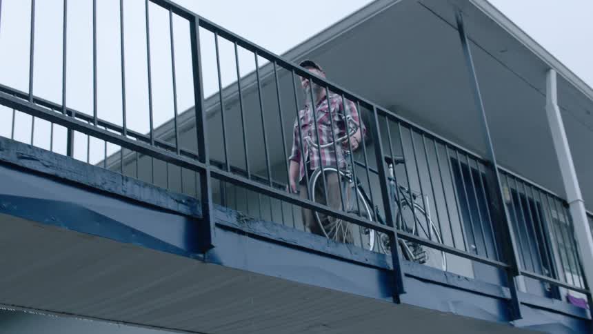 A man walking his bike over a walkway attached to a building
