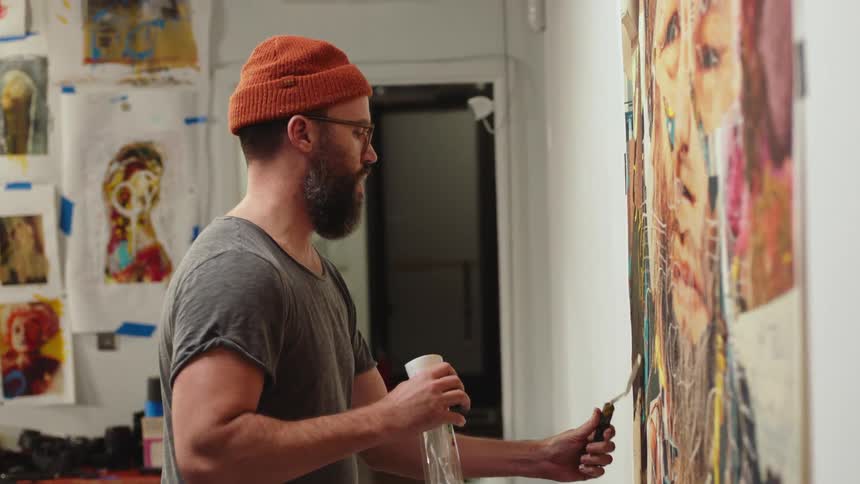 An artist is standing in an apartment while painting a large abstract painting on a large canvas