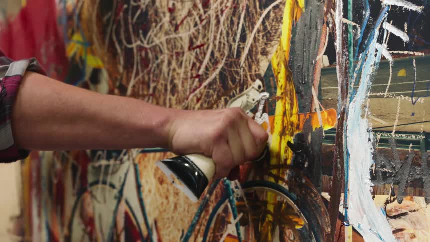 A persons hand squeezing a tube of paint on a painting