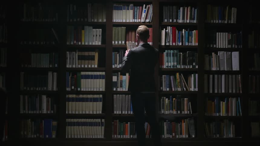 A man approaches a wall of bookshelves and removes a book