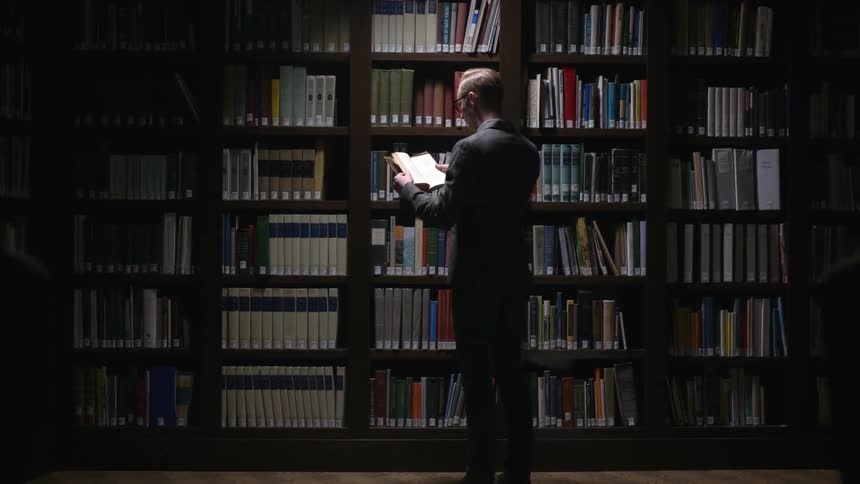 A man opens a book in a library