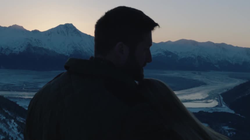 A man and woman standing before a view of a snowy landscape hold each other