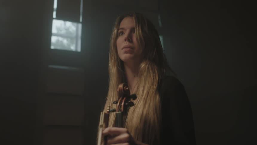 A woman stands in a room with her musical instrument