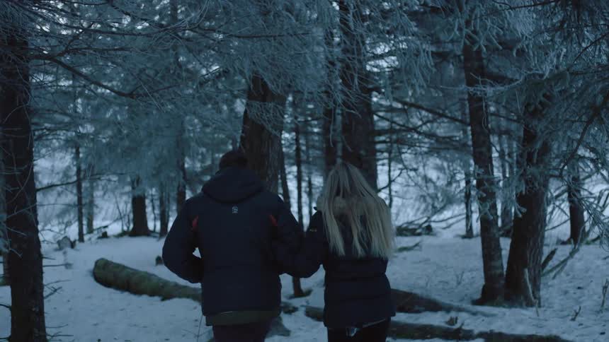 A man and woman walk through a snowy forest