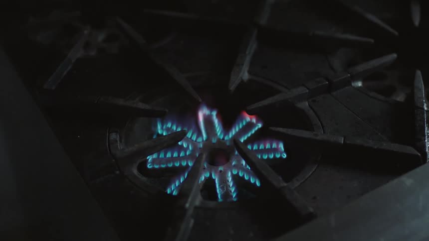 Blue flames emerge from the burner of a gas stove