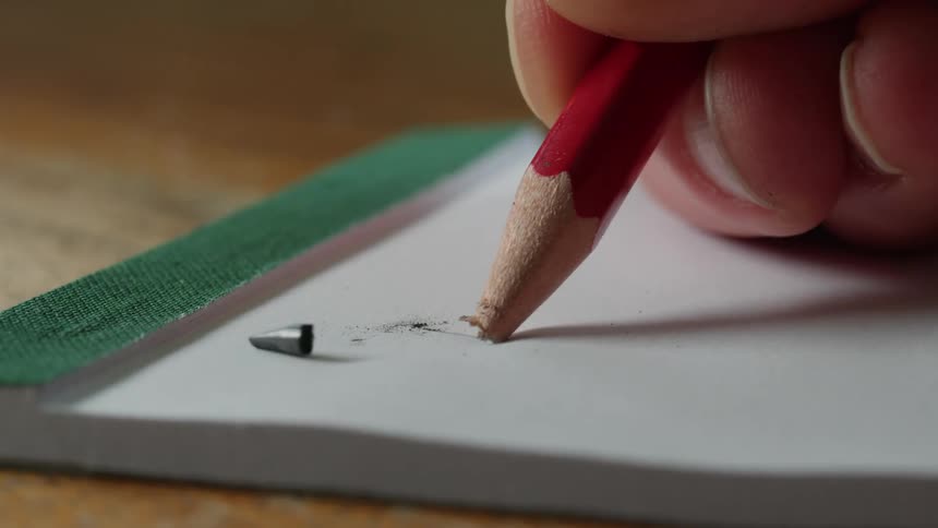 Close up of the tip of a pencil breaking over a white notepad