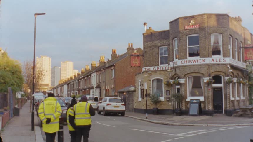 Three people standing in yellow jackets near a street and buildings