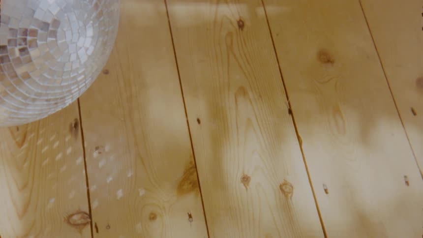Shadows and sunlight play on wooden boards over squares of light reflected from mirror ball