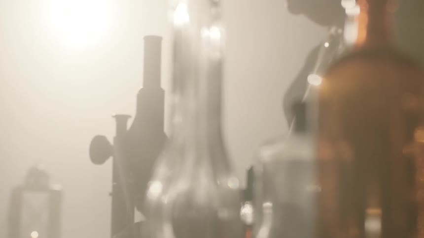 Sunlight streams through lab bottles and containers as a man approaches a microscope