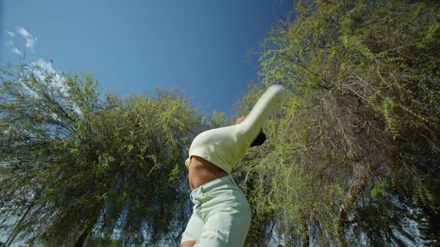 A woman in a yellow shirt dancing and moving her body under trees