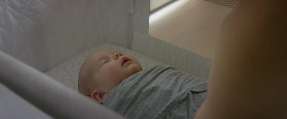 Infant boy wrapped in a baby blanket being placed in bassinet