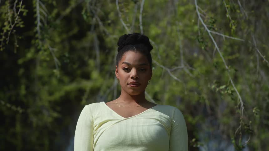 A woman standing in front of trees looking straight ahead