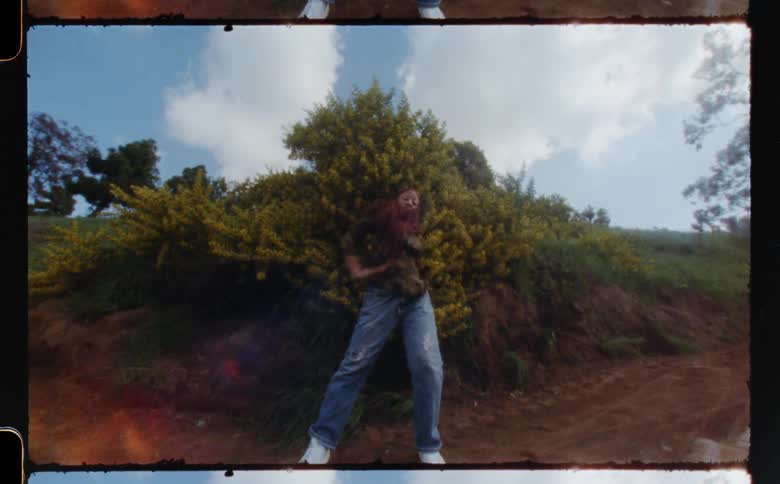 A young woman dances in front of a dirt hill