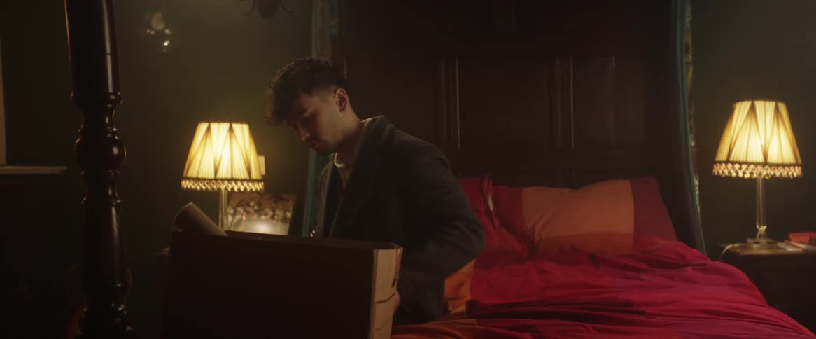 A man sitting on the edge of a bed putting things into a cardboard box