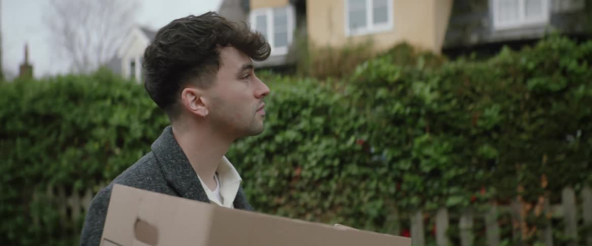 A man carries a paper bag with groceries down a neighborhood street