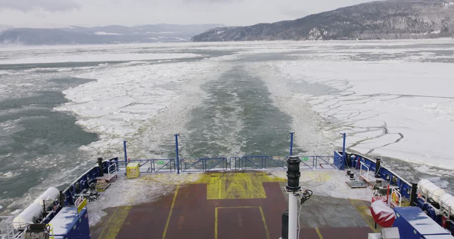 The back of a freight ship traveling through icy waters with mountains in the distance
