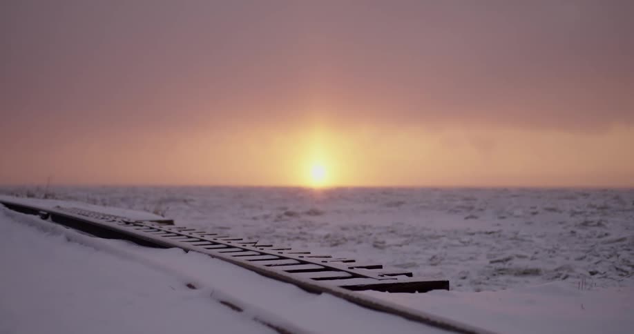 Snow covered train tracks in a field against red glow of the sunrise