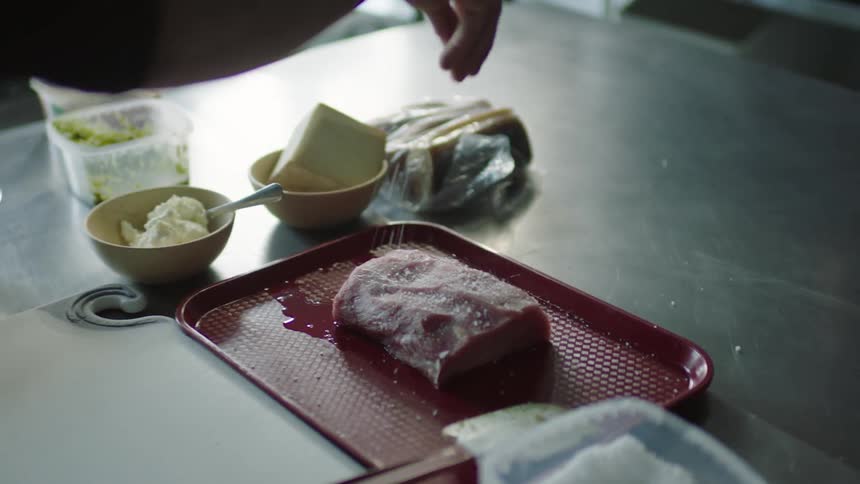 A person sprinkles salt over meat on a red tray