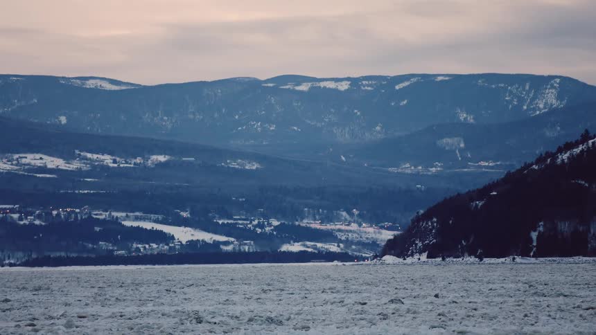 Slushy water moves slowly near forest covered mountains and town