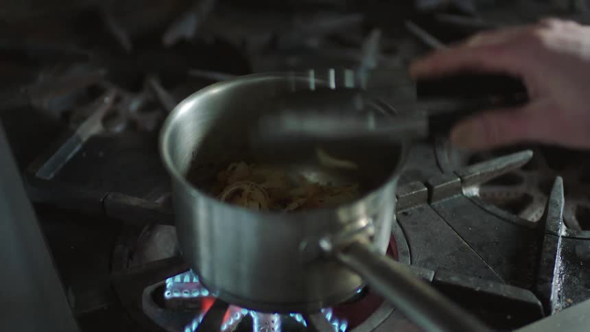 A pot on a stove with food in it a person stirs the food with tongs