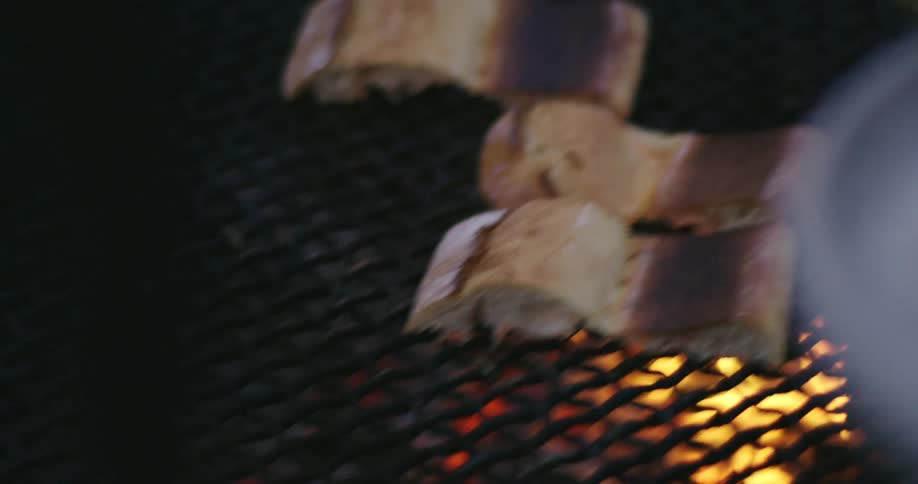 An up close of bread on a plate and a persons hand laying bread on a flaming grill