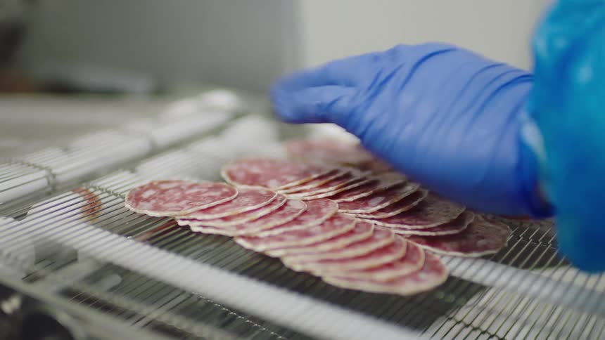 Food coming out of a conveyor as a person with blue gloves organizes and move the food