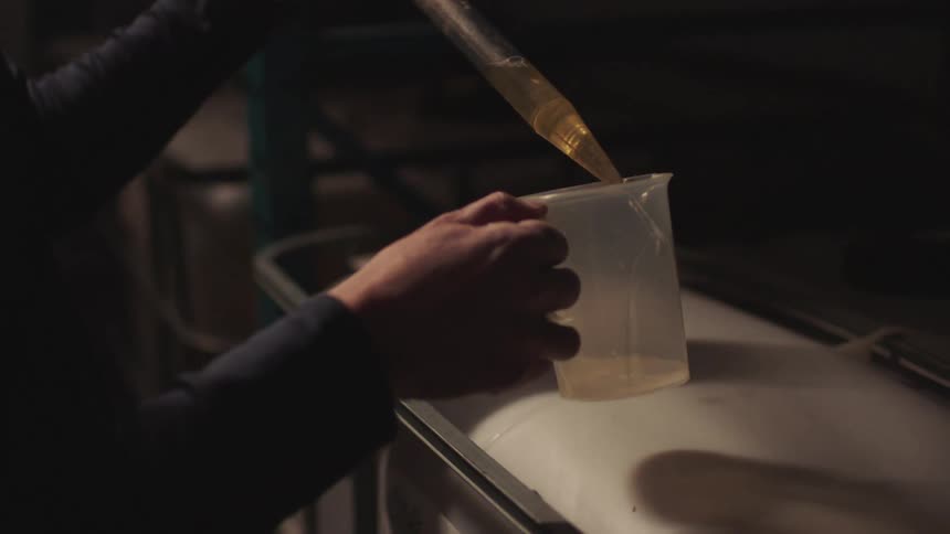 Person fills small pitcher with large dropper while standing near shelving