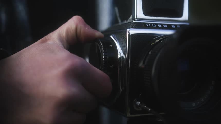 A mans hand turns a dial on analog medium format photo camera with a large lens