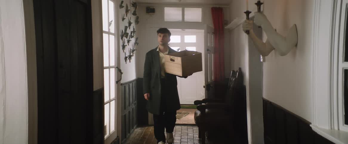 Young man walks into home entryway carrying cardboard box