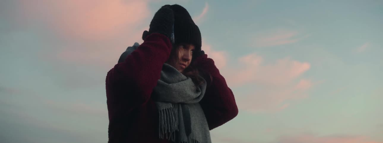 Woman standing outside bundled up in cold weather attire touches hat