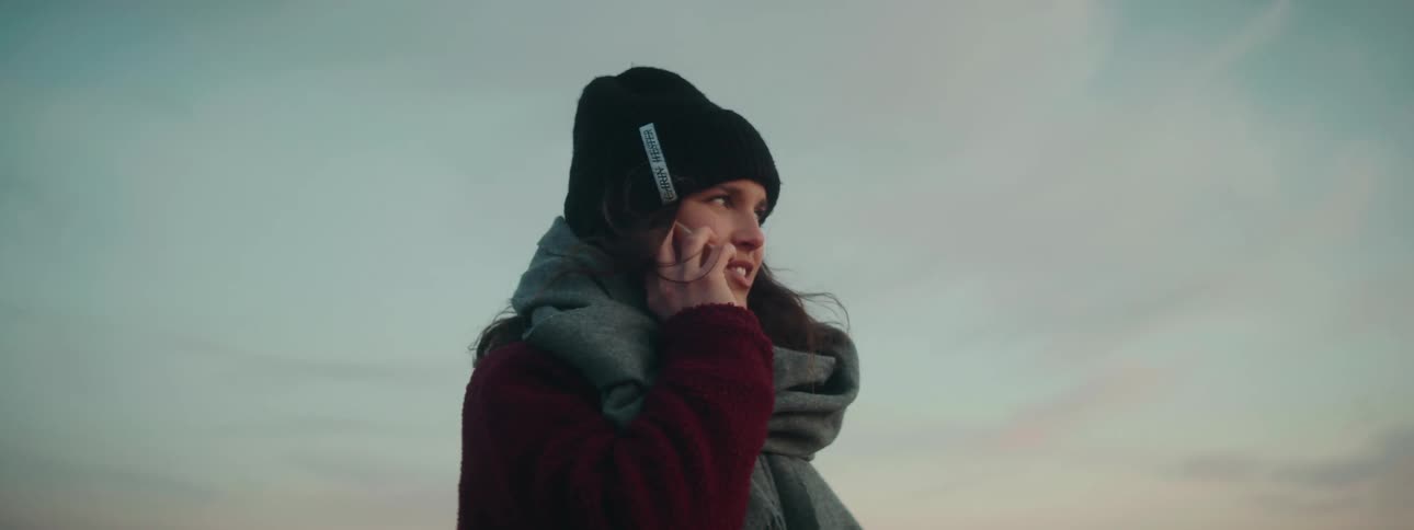 Woman bundled up against the cold smiles while talking on the phone outdoors