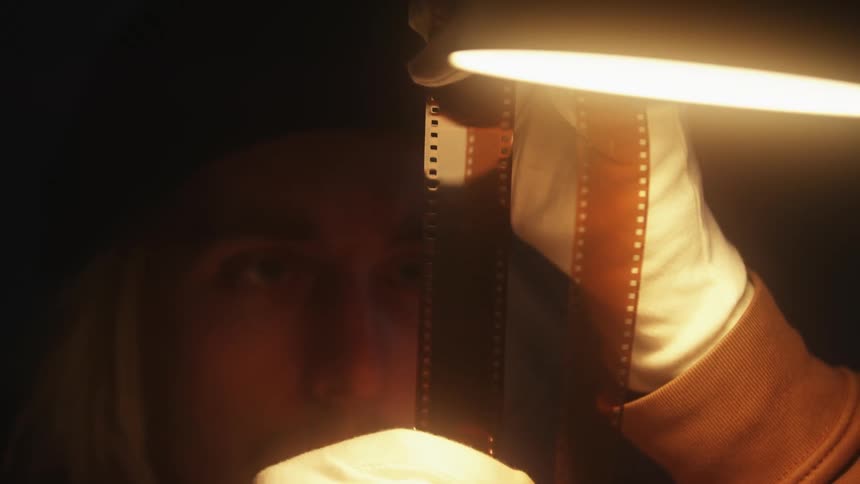 A close up of a man looking at old film with gloves on under a bright light