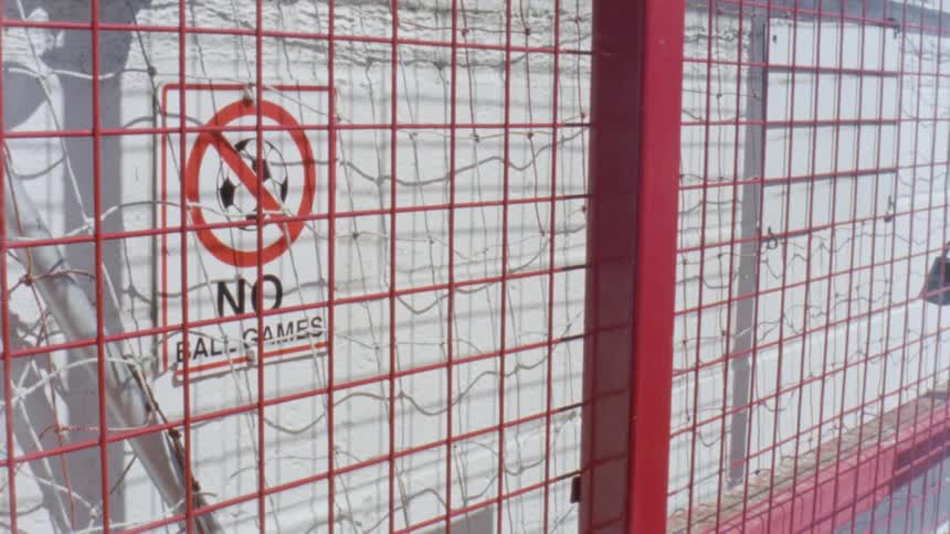 A sign by a fence warns that no ball games are allowed on the property