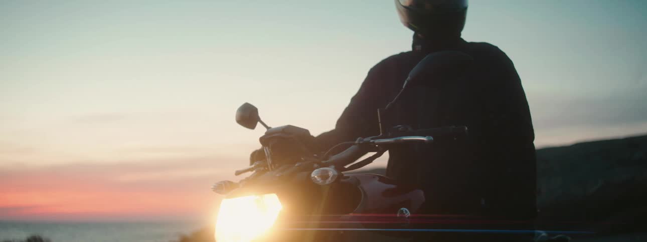 Person sitting on motorcycle on lookout point over ocean viewing sunsetsunrise