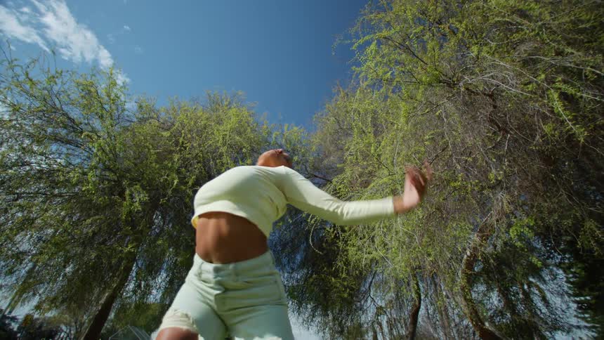 Woman wearing cropped top dances near trees under a cloudy sky