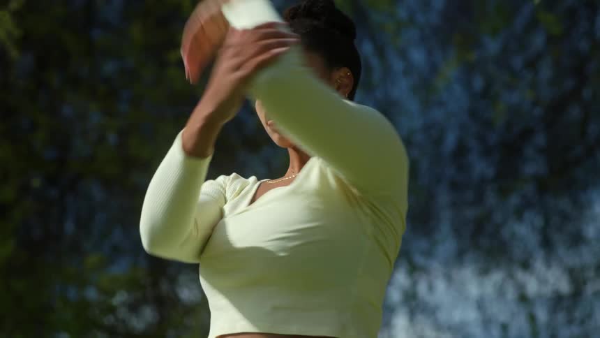 Woman dances outdoors under trees while wearing a crop top