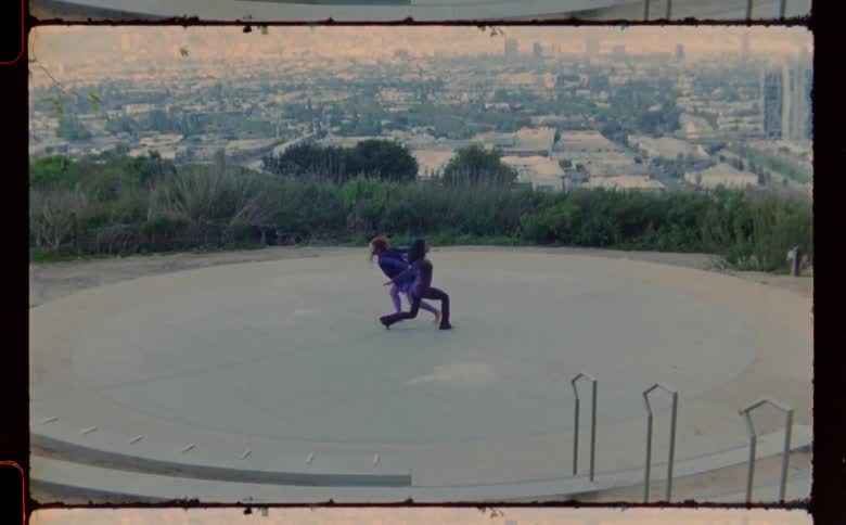 Two young women are performing a dance routine on a concrete platform that overlooks a large city