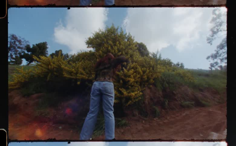 Woman with brown shirt jeans and a pair of white shoes dances on dirt road