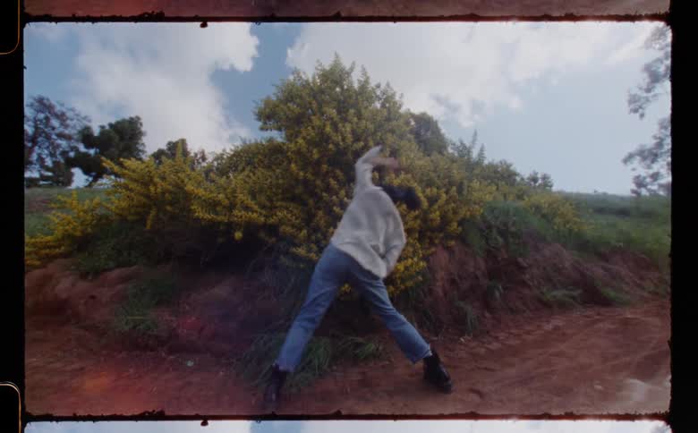Woman with gray shirt jeans and black boots dances on dirt road in the field