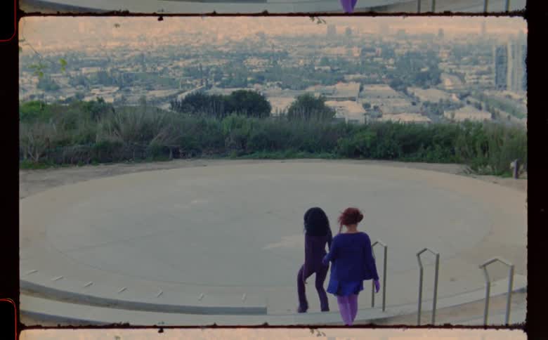 Two women walk down outdoor staircase onto round platform overlooking city then separate