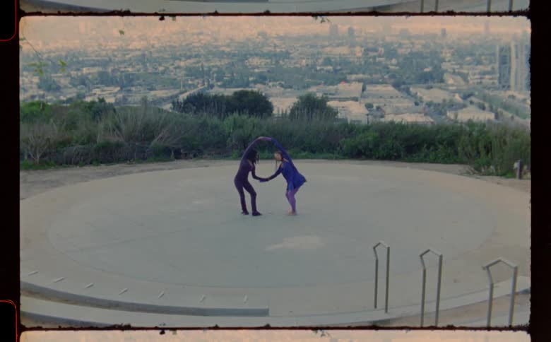 Two young women are performing a routine on a concrete platform overlooking a large city