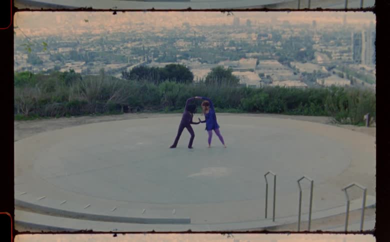 Two teenage girls are dancing in a park and the neighborhood buildings are in the distance