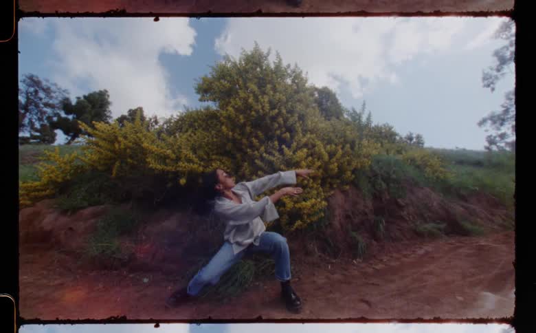 Woman in gray shirt jeans and black boots dances on dirt road in the open field