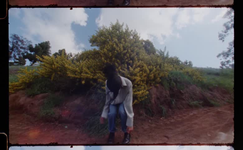 Woman with gray shirt jeans and black boots dances on dirt road in the field