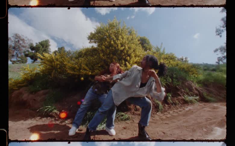 Two women dancing together in front of a large bush outside
